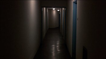 Movie still from “Caché” (2005), directed by Michael Haneke – An empty hallway with lights on and a blue door; Extreme Wide shot, High angle