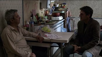 Movie still from “Caché” (2005), directed by Michael Haneke – Two people sitting at a table in a kitchen; Medium shot, Over the shoulder angle