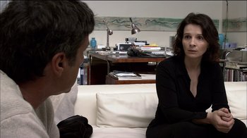 Movie still from “Caché” (2005), directed by Michael Haneke – A man and a woman sitting on a white couch in a room; Medium shot, Over the shoulder angle