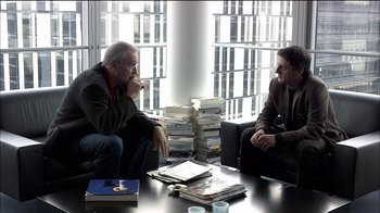 Movie still from “Caché” (2005), directed by Michael Haneke – Two men are sitting at a table talking to each other; Medium shot, High angle