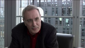 Movie still from “Caché” (2005), directed by Michael Haneke – An older man wearing glasses and a red shirt; Close Up shot, Over the shoulder angle