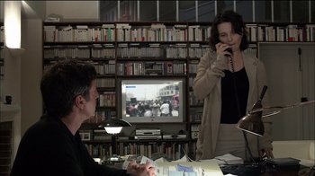 Movie still from “Caché” (2005), directed by Michael Haneke – A woman talking on a phone while a man sits at a table; Medium shot, Over the shoulder angle