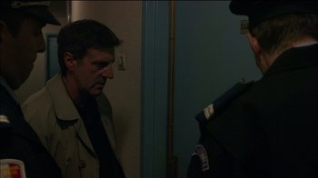 Movie still from “Caché” (2005), directed by Michael Haneke – A man wearing a suit and tie standing next to a police officer; Medium shot, Over the shoulder angle