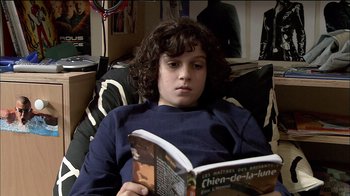 Movie still from “Caché” (2005), directed by Michael Haneke – A young boy is reading a book on the couch; Medium shot, High angle