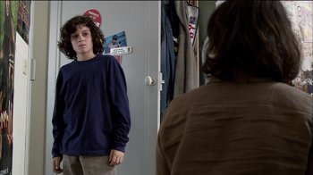 Movie still from “Caché” (2005), directed by Michael Haneke – A young boy standing in front of a mirror looking at himself in the mirror; Medium shot, Over the shoulder angle