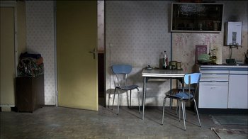 Movie still from “Caché” (2005), directed by Michael Haneke – A table and two chairs in an empty room; Wide shot, High angle