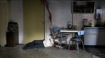 Movie still from “Caché” (2005), directed by Michael Haneke – A man laying on the floor of a room with blood on the floor; Wide shot, High angle