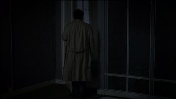 Movie still from “Caché” (2005), directed by Michael Haneke – A man in a trench coat standing in front of a window; Wide shot, High angle