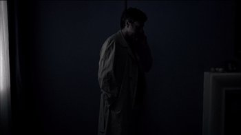 Movie still from “Caché” (2005), directed by Michael Haneke – A man standing in the dark talking on a cell phone; Medium shot, High angle