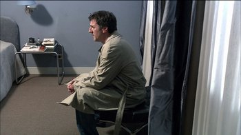 Movie still from “Caché” (2005), directed by Michael Haneke – A man sitting on a chair in front of a curtain; Medium shot, Over the shoulder angle
