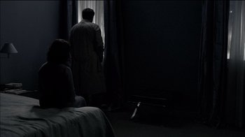 Movie still from “Caché” (2005), directed by Michael Haneke – A man standing in front of a window in a dark room; Wide shot, Over the shoulder angle