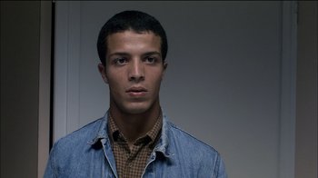 Movie still from “Caché” (2005), directed by Michael Haneke – A young man wearing a jean jacket and a plaid shirt; Close Up shot, Low angle