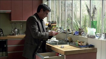 Movie still from “Caché” (2005), directed by Michael Haneke – A man in a suit and glasses is fixing a faucet; Medium shot, Low angle