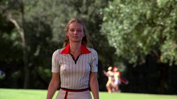 Movie still from “Caddyshack” (1980), directed by Harold Ramis – A woman in a white and red striped shirt is standing in the grass; Medium shot, Low angle