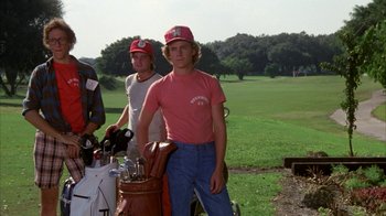 Movie still from “Caddyshack” (1980), directed by Harold Ramis – A man standing next to another man holding a bag of golf clubs; Medium shot, Low angle