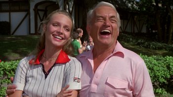 Movie still from “Caddyshack” (1980), directed by Harold Ramis – An older man and a young woman smiling for the camera; Close Up shot, Low angle