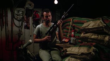 Movie still from “Caddyshack” (1980), directed by Harold Ramis – A man holding a rifle in a room filled with stacks of bags; Medium shot, Low angle