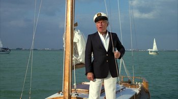 Movie still from “Caddyshack” (1980), directed by Harold Ramis – An older man wearing a sailor's hat standing next to a sail boat; Medium shot, Low angle