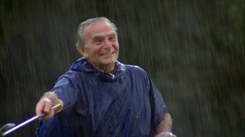Movie still from “Caddyshack” (1980), directed by Harold Ramis – An older man in a raincoat holding a frisbee in the rain; Medium shot, Low angle