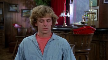 Movie still from “Caddyshack” (1980), directed by Harold Ramis – A young man with long blonde hair is sitting in a chair; Close Up shot, Over the shoulder angle