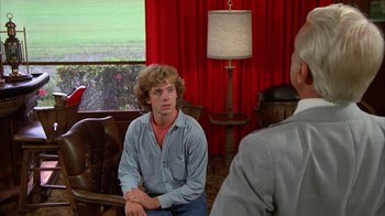 Movie still from “Caddyshack” (1980), directed by Harold Ramis – A man sitting on a chair in front of another man in a room; Medium shot, Over the shoulder angle