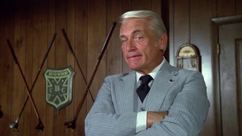 Movie still from “Caddyshack” (1980), directed by Harold Ramis – An older man wearing a suit and tie with his arms crossed; Close Up shot, Low angle