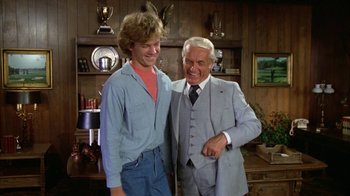 Movie still from “Caddyshack” (1980), directed by Harold Ramis – A man in a suit and tie standing next to a young man; Medium shot, Low angle