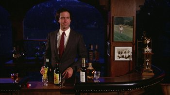 Movie still from “Caddyshack” (1980), directed by Harold Ramis – A man standing at a bar holding a bottle of wine; Medium shot, Low angle