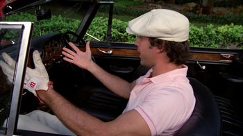 Movie still from “Caddyshack” (1980), directed by Harold Ramis – A man driving a car wearing a white hat; Medium shot, Over the shoulder angle