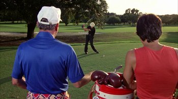 Movie still from “Caddyshack” (1980), directed by Harold Ramis – A man swinging a golf club on a golf course; Medium shot, Over the shoulder angle