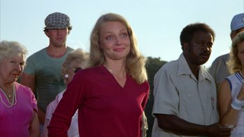 Movie still from “Caddyshack” (1980), directed by Harold Ramis – A woman in a red shirt is standing in front of a group of people; Medium shot, Low angle