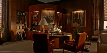 Movie still from “Café Society” (2016), directed by Woody Allen – A man sitting at a desk in a room with wooden paneled walls; Wide shot, High angle