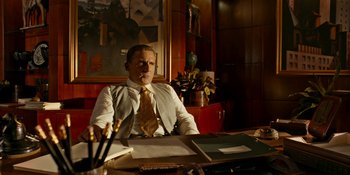 Movie still from “Café Society” (2016), directed by Woody Allen – A man sitting at a desk in front of papers and pens; Medium shot, Over the shoulder angle
