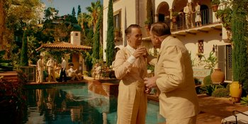 Movie still from “Café Society” (2016), directed by Woody Allen – Two men standing next to each other in front of a swimming pool; Wide shot, Over the shoulder angle