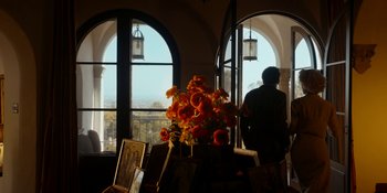 Movie still from “Café Society” (2016), directed by Woody Allen – A man standing in front of a vase of flowers in front of a window; Extreme Wide shot, Low angle