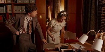 Movie still from “Café Society” (2016), directed by Woody Allen – A man and a woman standing next to each other in front of boxes; Medium shot, High angle