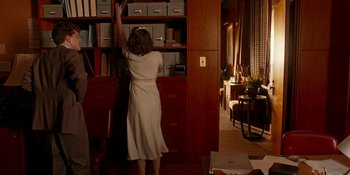 Movie still from “Café Society” (2016), directed by Woody Allen – A woman in a white dress reaching into a book case; Medium shot, Low angle