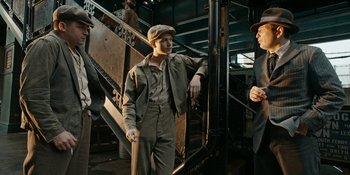 Movie still from “Café Society” (2016), directed by Woody Allen – A man in a suit and hat standing next to stairs; Medium shot, Low angle
