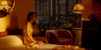 Movie still from “Café Society” (2016), directed by Woody Allen – A woman sitting on a bed drinking a cup of coffee; Wide shot, High angle