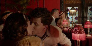 Movie still from “Café Society” (2016), directed by Woody Allen – A man and a woman kissing in front of other people in a restaurant; Medium shot, Over the shoulder angle