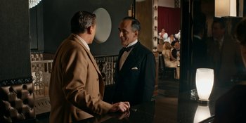 Movie still from “Café Society” (2016), directed by Woody Allen – Two men in suits talking to each other in front of a crowd; Medium shot, Over the shoulder angle