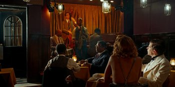 Movie still from “Café Society” (2016), directed by Woody Allen – A group of people sitting in front of a microphone; Extreme Wide shot, Over the shoulder angle