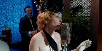 Movie still from “Café Society” (2016), directed by Woody Allen – A woman in a black hat is singing into a microphone; Close Up shot, Low angle
