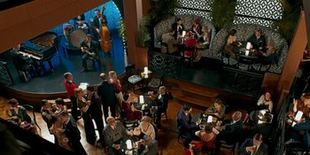 Movie still from “Café Society” (2016), directed by Woody Allen – A group of people sitting at tables in front of a stage; Extreme Wide shot, High angle