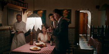 Movie still from “Café Society” (2016), directed by Woody Allen – A group of people standing around a table with food; Wide shot, Over the shoulder angle