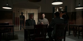 Movie still from “Café Society” (2016), directed by Woody Allen – A group of men sitting at a table in a room; Wide shot, Over the shoulder angle