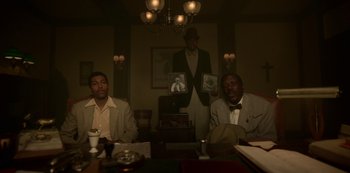 Movie still from “Fargo” (2014), created by Noah Hawley – Two men sitting at a dinner table holding up pictures; Medium shot, Low angle