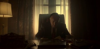 Movie still from “Fargo” (2014), created by Noah Hawley – A man sitting at a desk in front of a window; Medium shot, Low angle