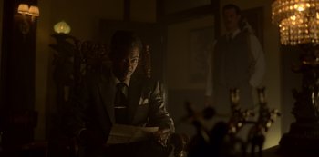 Movie still from “Fargo” (2014), created by Noah Hawley – A man sitting in a chair holding a paper; Medium shot, Low angle