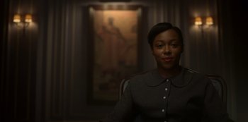 Movie still from “Fargo” (2014), created by Noah Hawley – A woman sitting in front of a painting in a dark room; Medium shot, Low angle